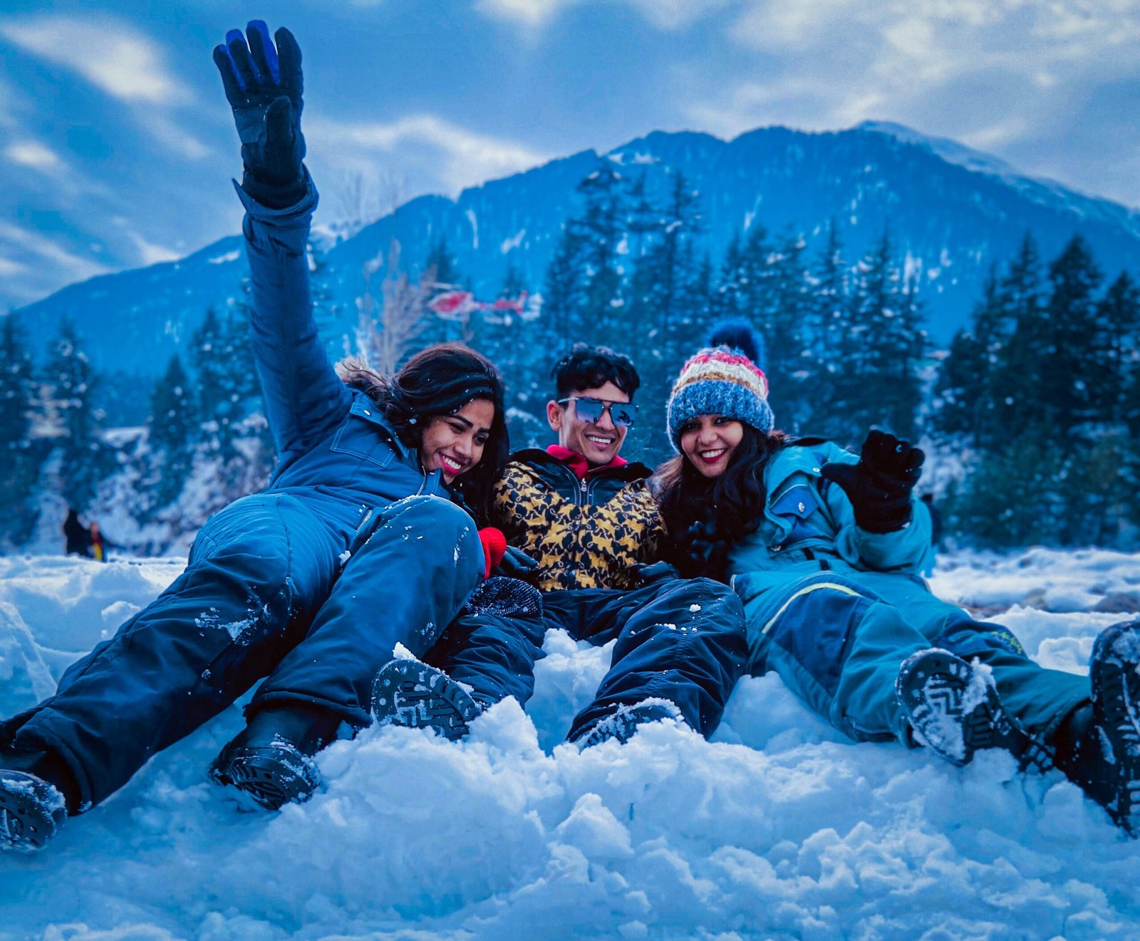 Friends enjoying snowfall in Manali, Himachal Pradesh with Himalayan mountains and pine trees during winter vacation in India